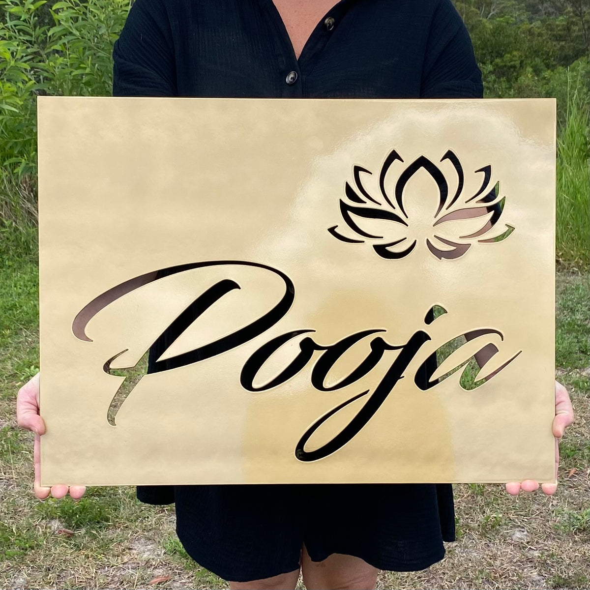 Person holding a sign with 'Pooja' and a lotus symbol outdoors.