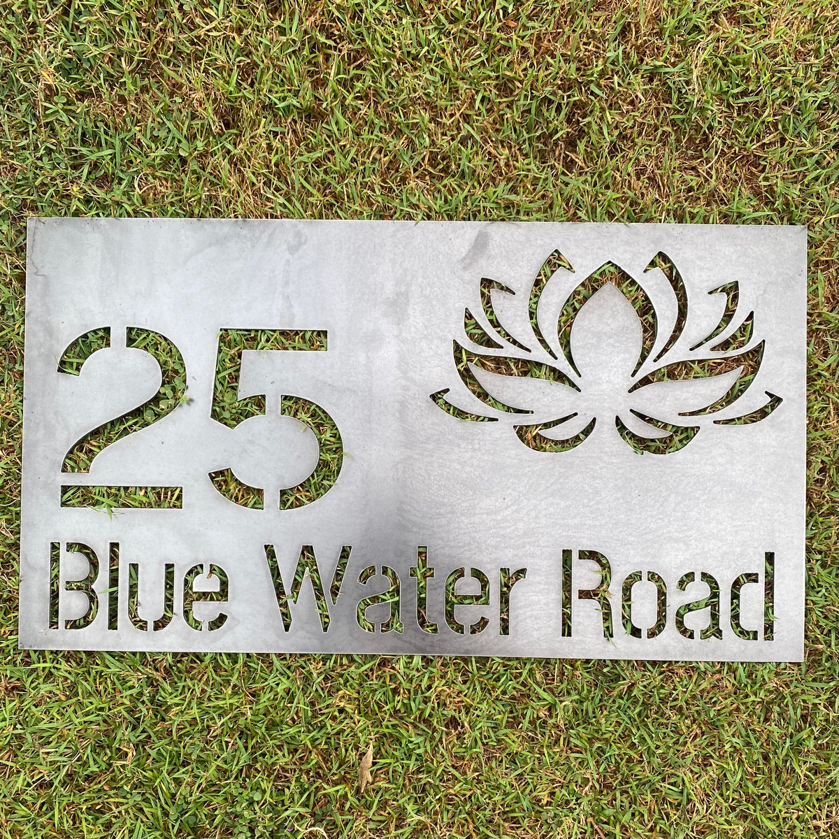 Metal sign with number 25, leaf design, and 'Blue Water Road' text on grass