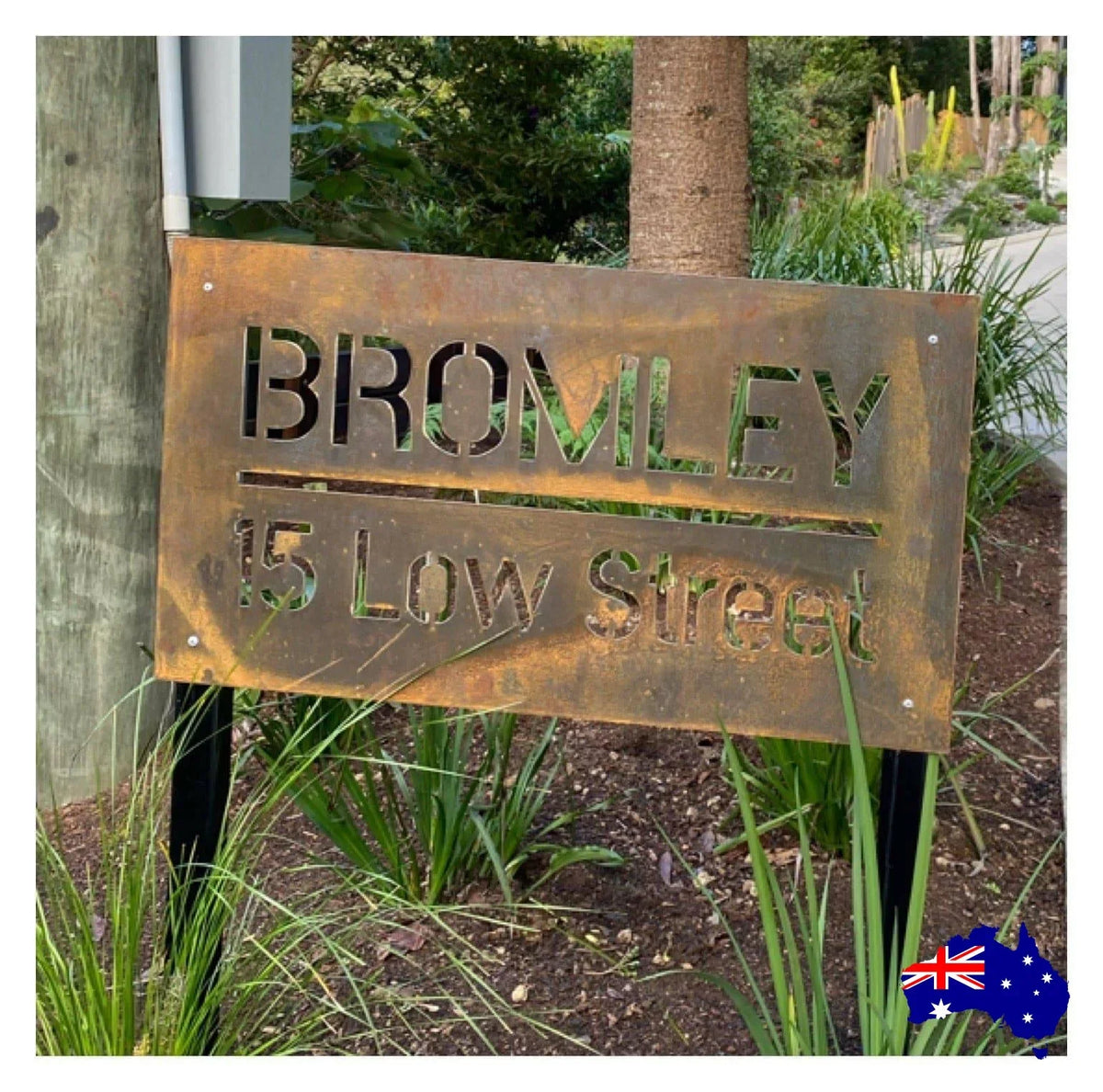 Rust-colored metal sign with 'Bromley 15 Low Street' text, set against a natural background with plants and trees.