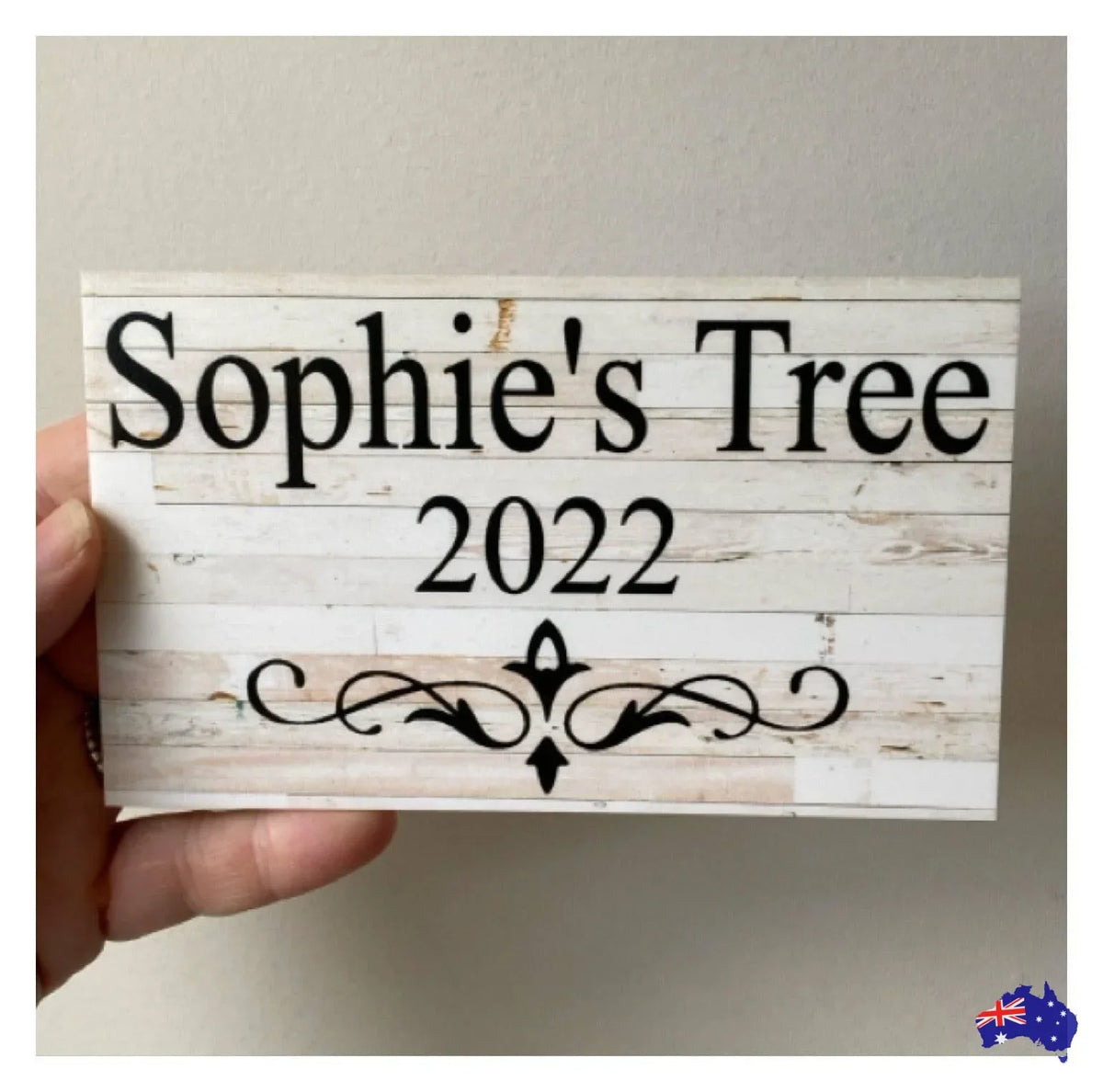 Wooden sign with 'Sophie's Tree 2022' text held by a hand against a plain background.