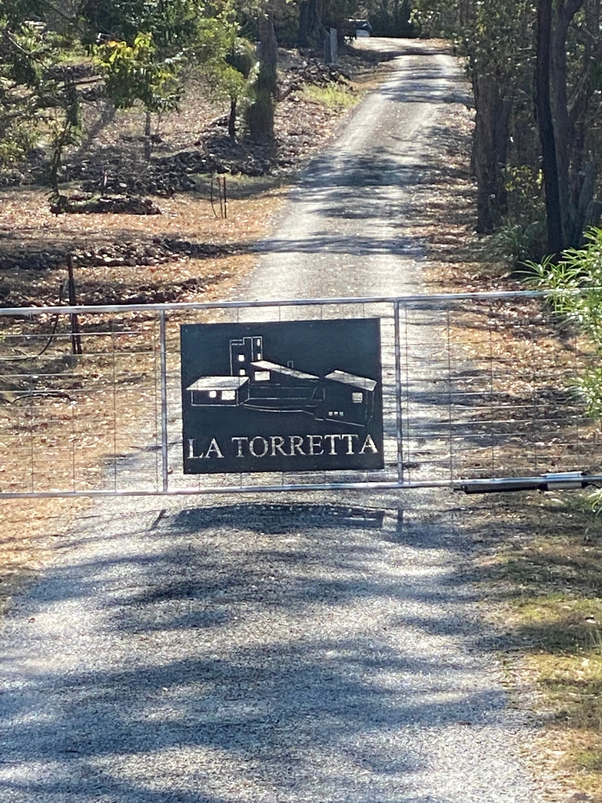 Metal sign with 'La Torretta' on a gravel path surrounded by trees