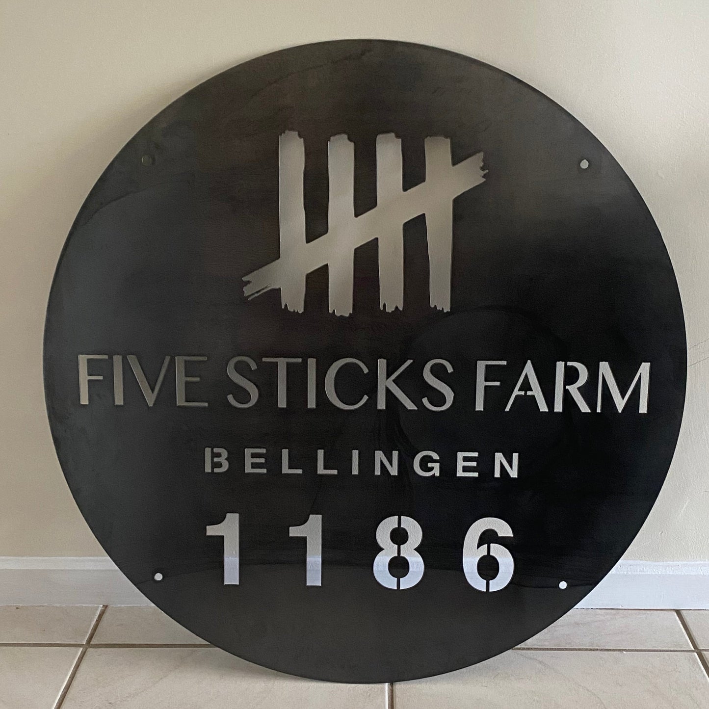 Round metal sign with 'Five Sticks Farm' branding on a tiled wall.