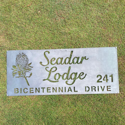 Metal sign for Seadar Lodge on Bicentennial Drive with a decorative plant design, placed on grass.