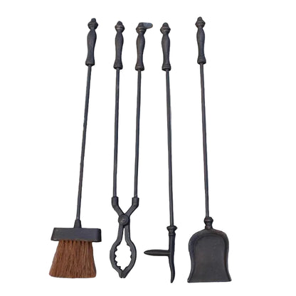 Set of black fireplace tools including a brush, tongs, and scoop on a stone wall background.