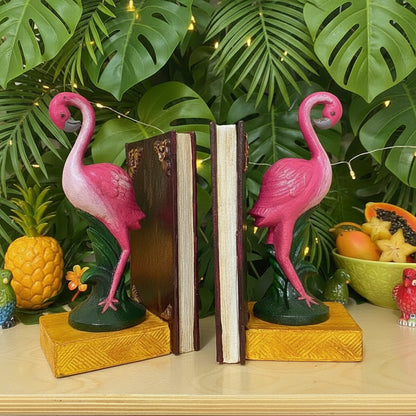 Pink flamingo bookends on a wooden surface with green foliage in the background