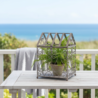 French Scroll terrarium with a potted fern on a white timber table on a Hamptons coastal veranda — antique grey iron garden decor