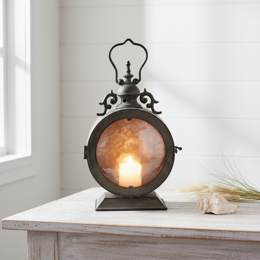Vintage metal and glass candle lantern with lit candle glowing amber, styled on a whitewashed timber table with shells and dune grass in a coastal Hamptons beach house - 34cm hurricane candle holder