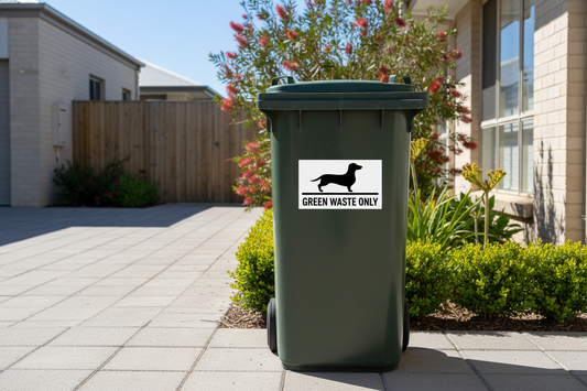 Green-lid organics wheelie bin with white background black text Dachshund sticker reading Green Waste Only — rubbish bin sticker applied outdoors, Aussie made