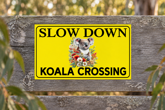 Slow Down Koala Crossing sign on a weathered roadside timber fence